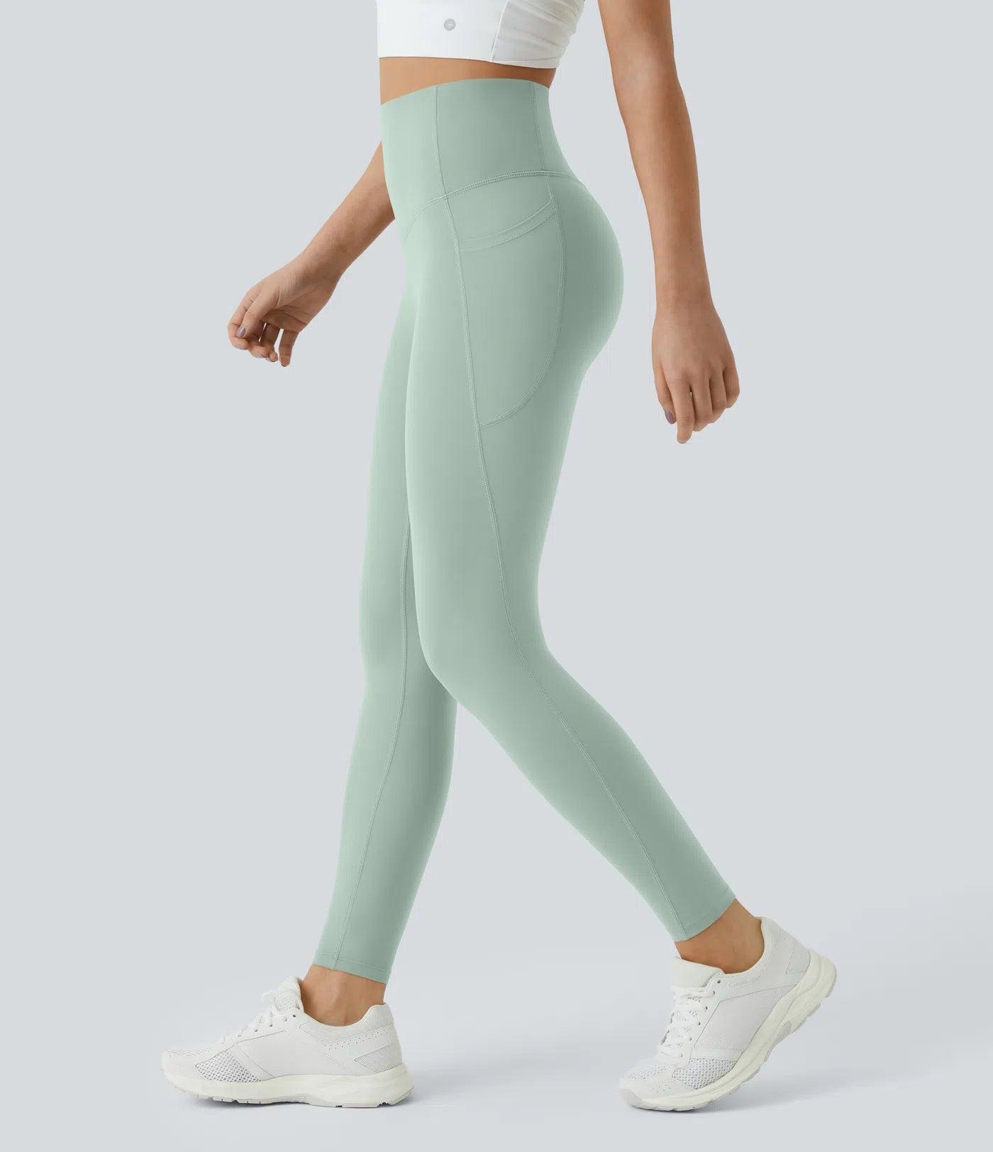 Person wearing light green leggings and white sneakers on a plain background